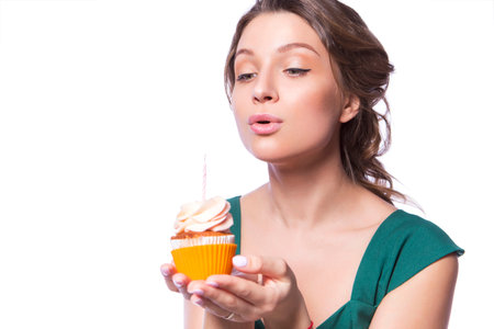 Brunette pretty beautiful caucasian woman in green festive dress blowing candle on a birthday party cupcake. Isolated white backgroundの写真素材
