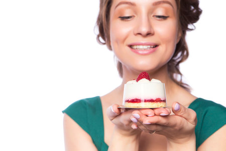 Brunette pretty beautiful caucasian woman in green festive dress showing proposing holding sweet cupcake dessert in her palms. Isolated white backgroundの写真素材
