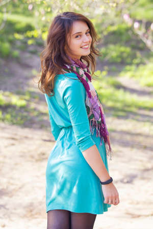 Cute ordinary caucasian brunette woman in casual outfit walking at the nature park, posing sensually in flowers. Cold spring (autumn) weather, warm dress on a girl. Sunset. Copy spaceの写真素材