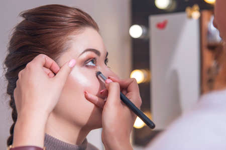 Cute beautiful young caucasian brunette woman with evening make up in casual outfit posing with neutral emotions. Mirror with lights on a background. Close up of a fresh clean face skin. Copy spaceの写真素材