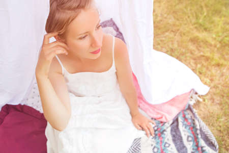 Cute happy caucasian woman with short haircut in white dress in park relaxing feeling good, smiling. Summer sunset, outdoors. Copy spaceの写真素材
