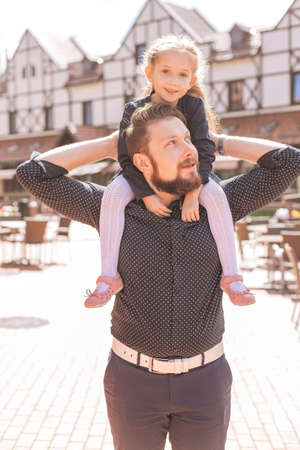 Daughter sitting on fathers shoulders. They on a summer walk in european cityの写真素材