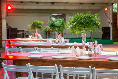 Decoration for a wedding ceremony on a back yard with tables, plates, and vases full of anthurium...