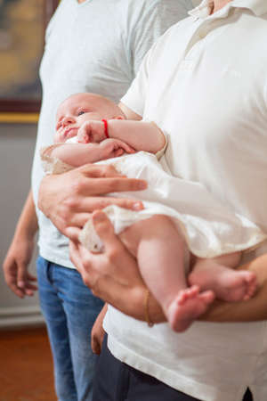 Mother (caucasian young woman) holding little infant kid in baptism (christening) ceremony in churchの写真素材