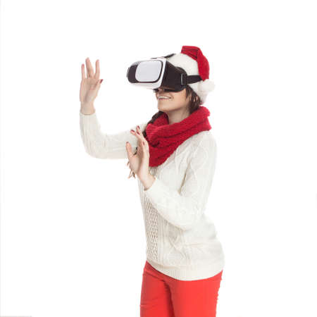 Cute teenage girl with long dark hair standing on a white background in white sweater and red santa...