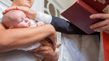 Godfather (caucasian young man) holding little infant kid in baptism (christening) ceremony in churchの写真素材