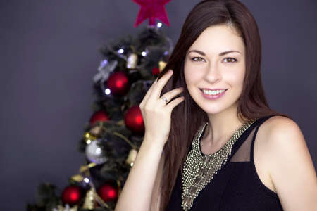 Cute smiling woman in evening sexy dress standing near New Year tree, giving a present on a isolated white backgroundの写真素材