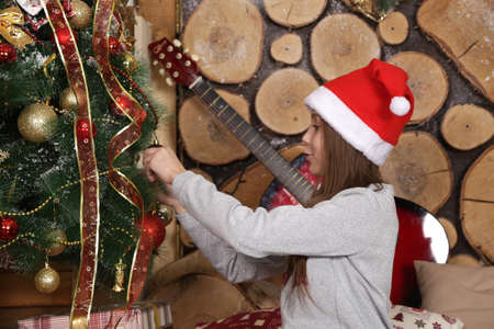 girl in a red cap decorates a Christmas tree in a festive interiorの写真素材