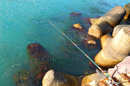 spinning rod for fishing against a background of sea water and coastal stones close-upの写真素材