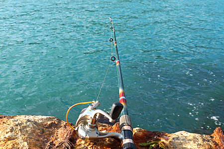 spinning rod for fishing against a background of sea water and coastal stones close-upの写真素材