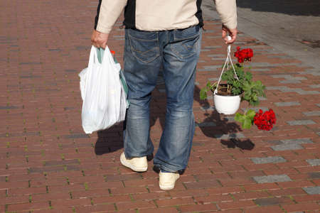 a man walks down the street with a full package and flowers in a flower pot, rear view.