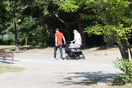 young couple walks in the park with twins in a stroller