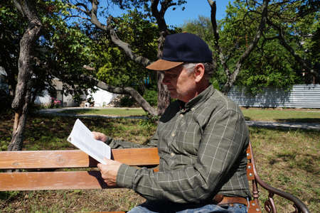 man reads a book on a park bench in summer.