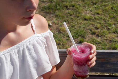 refreshing fruit drink with a straw in the hands of a girl in the park.の写真素材