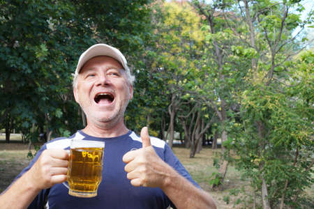 a laughing man holds a mug of beer in one hand, with the other hand shows that everything is fine in...