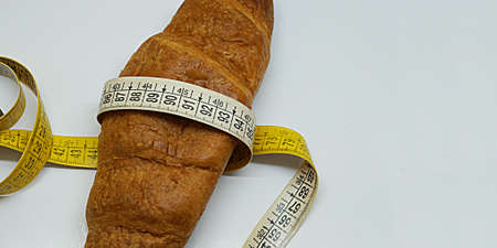 soft measuring ruler wrapped around a croissant as a symbol of unhealthy nutrition, copy spaceの写真素材