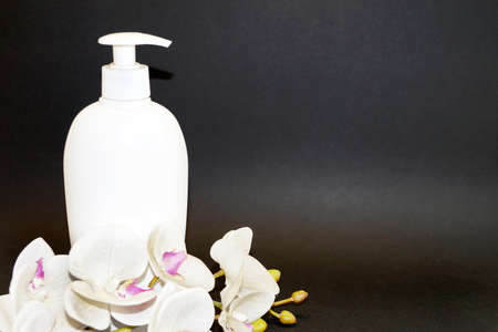 white cosmetic bottle and white orchid flower on a black background close upの写真素材