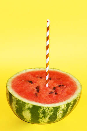 half watermelon with cocktail straw on yellow background, close-up