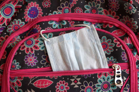 a medical mask sticking out of a school backpack close up