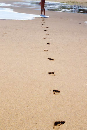 feet of a young girl walk barefoot on a wet beach, leaving footprints in the sand.の写真素材