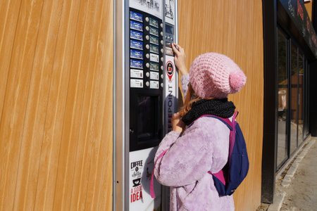 Varna, Bulgaria - November, 26, 2020: teen girl in a medical mask buys a drink from a vending machine on the streetのeditorial素材