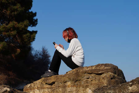 teenage girl sitting on a stone and listening to music on headphones.