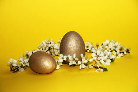 golden eggs and flowering branch on yellow background, easter conceptの写真素材