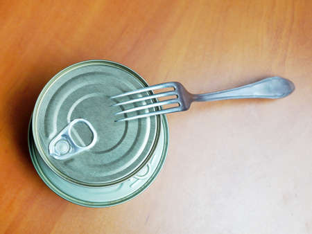 closed tin can and fork on wooden table.の写真素材