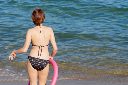 Teenage girl in a swimsuit with a bathing noodle goes to the sea.の写真素材