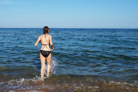 teenage girl running into the sea back view.の写真素材