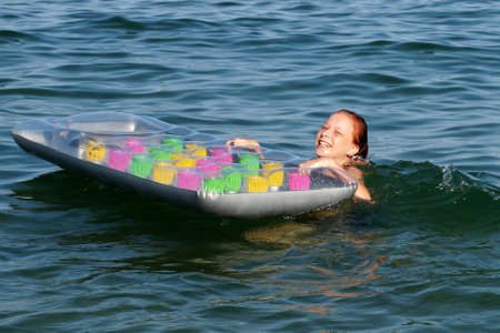 teenage girl holding an inflatable mattress in the water and laughing.