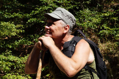 adult smiling man leaning on a stick surveys the surroundings.