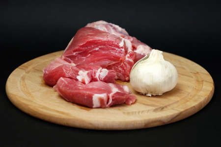 pork meat and garlic on a round wooden board on a black background.の写真素材