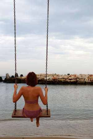 Teenage girl in swimsuit swinging on seashore, back view.