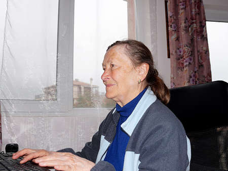portrait of a smiling elderly woman sitting at a computer.の写真素材