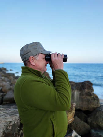 an adult man looks at the sea horizon with binoculars.の写真素材