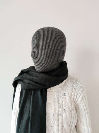 girl with a closed knitted fabric face in a white sweater and black scarf.の写真素材