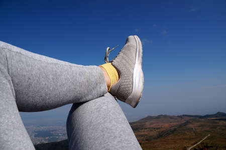 legs of a resting woman in sneakers against the background of the sky and mountains.