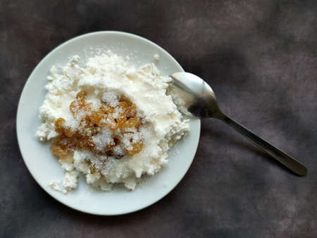 cottage cheese with raisins on a plate with a spoon on a dark vintage background, top view