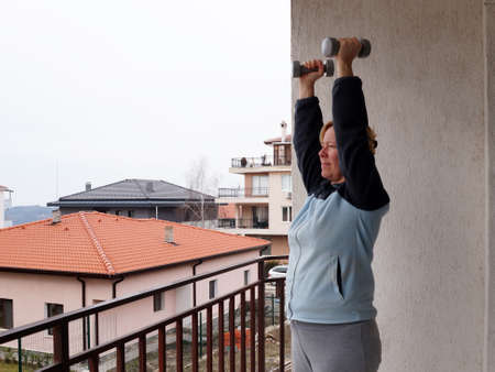 home sports training, adult woman performs exercises with dumbbells on the balcony.