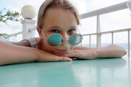 smiling teen girl in sunglasses at the table put her head in her hands.の写真素材