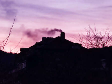 smoke from the chimney on the roof of the house against the sunset purple sky.