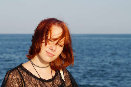 portrait of a smiling red-haired teenage girl against the backdrop of the sea.の写真素材