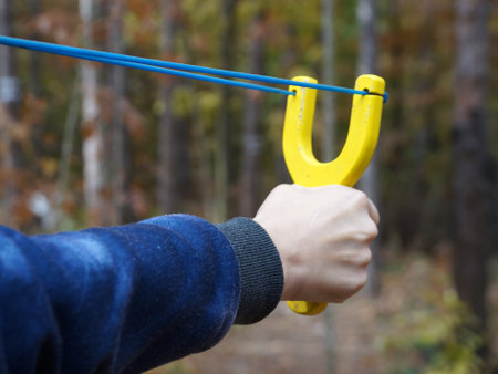 slingshot with a stretched bowstring in a female hand against the backdrop of a forestの写真素材