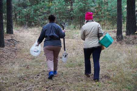 two women with baskets and a shovel go to the forest, rear view.
