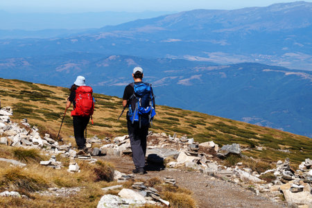 Man and woman with backpacks and walking sticks walking through the mountains, rear view.の写真素材