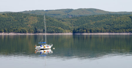 Yacht on a mountain lake, high shore reflected in the water.の写真素材