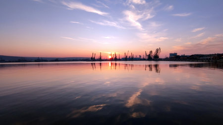 Panorama of Varna seaport at sunset, cargo cranes and pink clouds reflected in the waterの写真素材