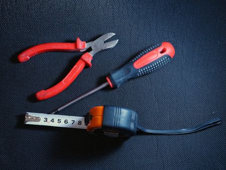 Tape measure, screwdriver and side cutters on black background, top view.
