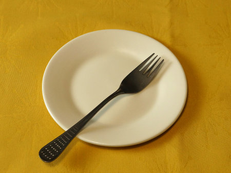 Close-up of a fork on a white plate on a yellow tablecloth.の写真素材
